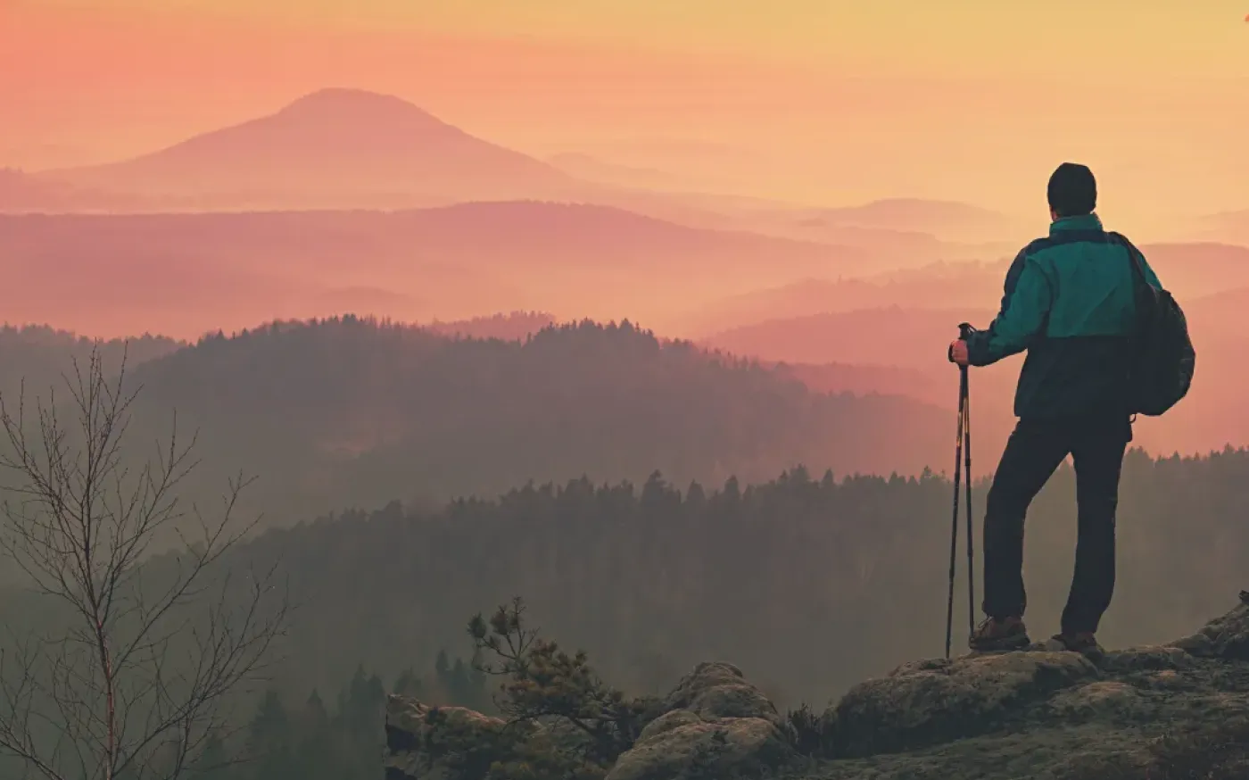 a man standing on top of a mountain, silhouetted against a vibrant sunset